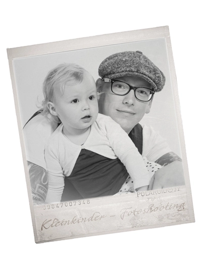 Schwarz-weißes Polaroid-Foto von einem lächelnden Vater mit Brille und Schiebermütze, der sein Kleinkind liebevoll im Arm hält. Ein emotionaler Moment eines Vater-Kind-Fotoshootings, festgehalten von Michael Schalansky Fotografie in Erfurt.